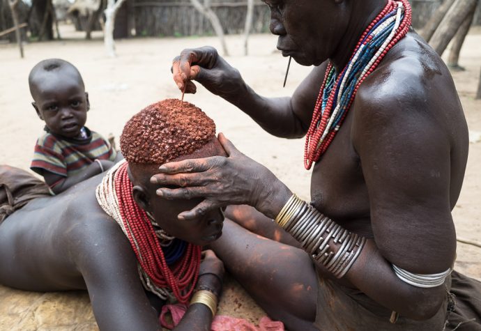 Ochre being applied to a woman from Karo tribe. South Omo region. Kolcho, Ethiopia. How To Visit South Omo, Ethiopia (Omo Valley) - GreatDistances / Matt Wicks