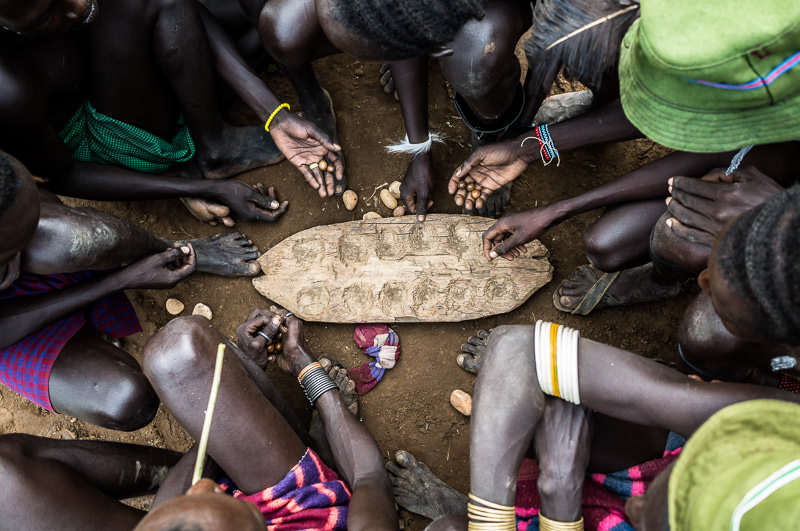 Men from the Dassenech tribe playing a traditional board game in Omorate. Photographing the Tribes of South Omo, Ethiopia - GreatDistances / Matt Wicks